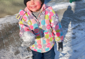 Dziewczynka stoi na placu zabaw i trzyma kulkę śniegu.