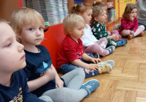 Dzieci siedzą na podłodze i biorą udział w zajęciach.