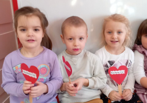 Dzieci trzymają papierowe serca z napisem: Kocham Cię!