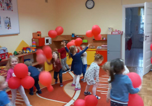 Dzieci podrzucają czerwone balony.