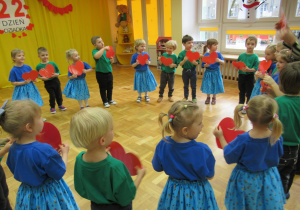 Dzieci stoją w kole trzymając w rączkach czerwone serduszka.