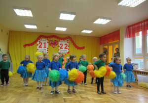 Dzieci stoją trzymając w rękach kolorowe pompony.