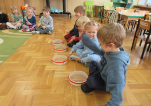 Dzieci siedzą na podłodze i grają na instrumentach.