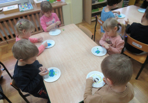 Dzieci siedzą przy stolikach i lepią z plasteliny.