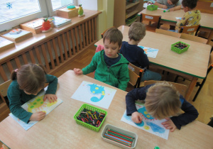 Dzieci siedzą przy stoliku i wykonuja prace plastyczne.