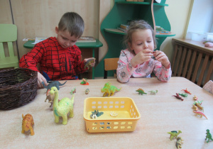 Chłopiec i dziewczynka bawią się figurkami dinozaurów.