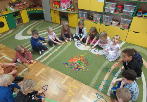 Dzieci siedzą w kole i układają figury z kolorowych patyczków.
