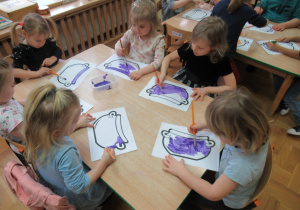 Dzieci siedzą przy stoliku i malują farbami.
