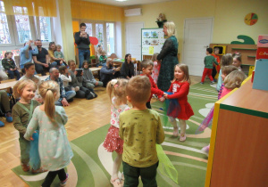Dzieci tańczą w małych kółeczkach, rodzice obserwują.