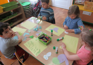 Dzieci siedzą przy stole i wykonują pracę plastyczną.