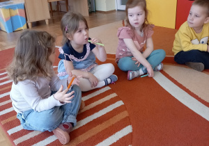 Dzieci siedza na dywanie i biorą udział w zajęciach.