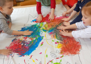 Przedszkolaki malują farbami z użyciem rąk.
