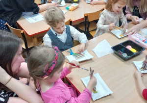Dzieci malują farbami drewniane zajączki.