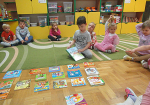 Dzieci siedzą na dywanie przed nimi leżą książki.