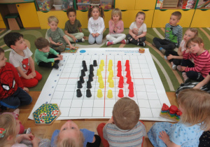 Dzieci siedzą wokół maty do kodowania, na macie ułożona flaga Belgii z kolorowych kubeczków.