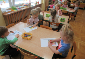 Dzieci siedzą przy stolikach i kolorują kredkami flagę Belgii.