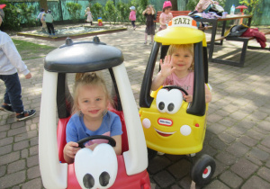 Dziewczynki siedzą w samochodzikach na placu zabaw.