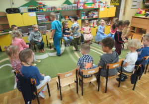 Dzieci siedzą na krzesłach ustawionych w okrąg.