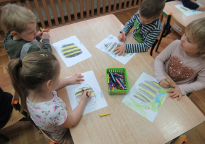 Dzieci siedzą przy stole i rysują pszczoły.