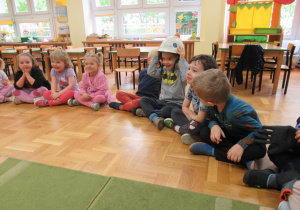 Dzieci siedzą na podłodze, chłopiec ma na głowie kask.