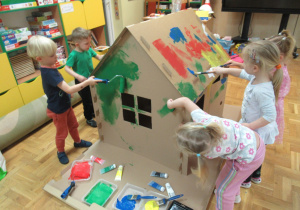 Dzieci malują dom farbami.