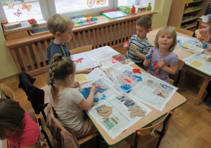Dzieci siedzą przy stole i malują farbami.