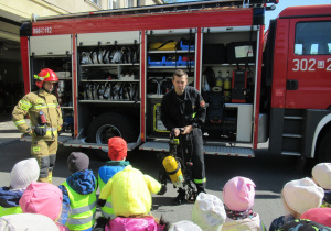 Panowie strażacy pokazują dzieciom sprzęt gaśniczy.