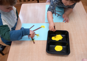Dzieci malują żółtą farbą kwiaty forsycji.