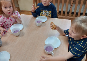 Dzieci siedzą przy stolikach i jedzą gofry belgijskie.