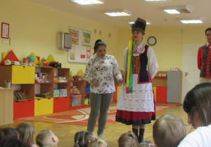 Pani stoi przed dziećmi w stroju kurpiowskim.