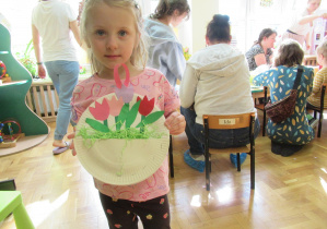 Dziewczynka pokazuje pracę plastyczną: tulipany w papierowym koszyku.