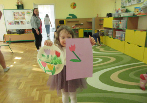 Dziewczynka pokazuje pracę plastyczną: tulipany w papierowym koszyku.