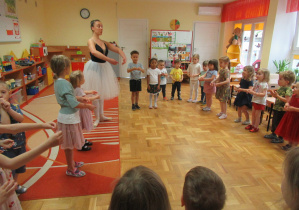 Pani w stroju baletnicy uczy dzieci tańczyć.
