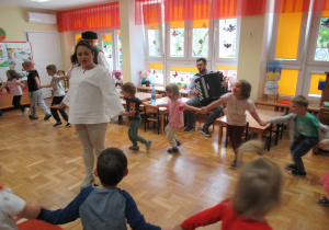 Dzieci tańczą w kole podczas koncertu, pan gra na akordeonie.