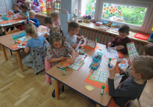 Dzieci przy stolikach wykonują prace plastyczne.