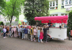 Dzieci stoją w kolejce przed kramem z lodami.