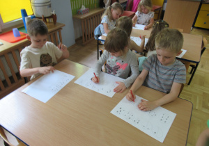 Dzieci siedzą przy stolikach i rysują.