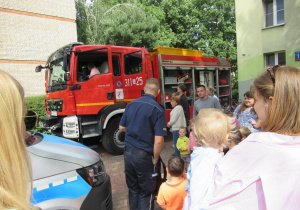 Dzieci i dorośli stoją przed wozem strażackim.