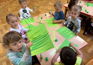 Dzieci przyklejają na kartkę, wycięte z papieru, zielone paski