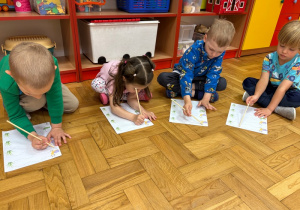 Dzieci wodzą po śladzie drewnianymi patyczkami