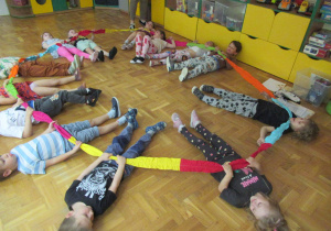 Dzieci leżą na podłodze i trzymają kolorową gumę.
