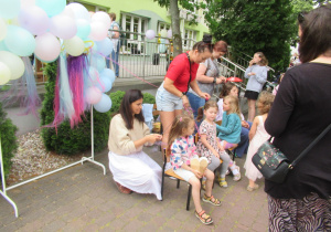 Panie zaplatają dzieciom kolorowe warkoczyki.