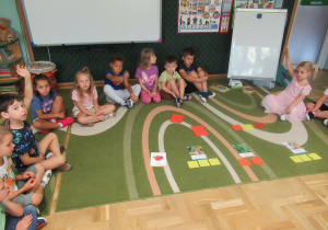 Dzieci siedzą na dywanie podczas zajęć edukacyjnych.