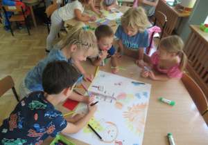 Dzieci rysują w małych grupach przy stolikach.