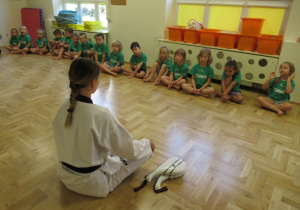 Dzieci siedzą w szeregu podczas zajęć z elementami teakwondo.