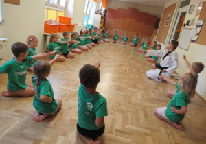 Dzieci siedzą w kole podczas zajęć z elementami teakwondo.