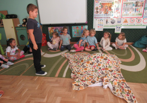 Dzieci siedzą na dywanie podczas zajęć dydaktycznych.