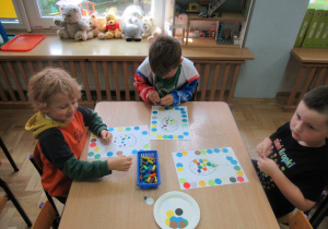 Dzieci przy stoliku wykonują prace plastyczne.
