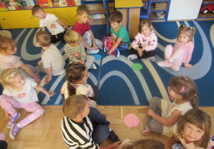 Dzieci siedzą na dywanie, przed nimi kółka z papieru.