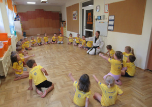 Dzieci siedzą w kole podczas zajęć z elementami teakwondo.